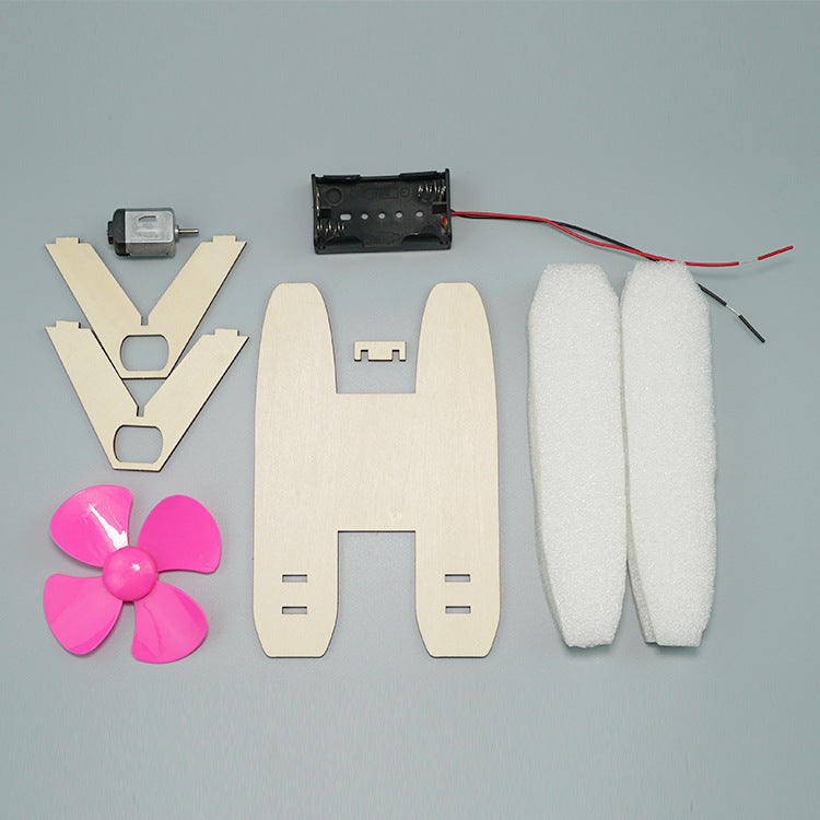 Unassembled parts of the DIY Hovercraft Kit, including wooden pieces, motor, propeller, battery case, and foam floats.
