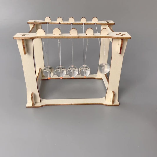 Assembled DIY Newton's Cradle Kit with five clear acrylic spheres swinging. Wooden base structure. Physics science toy for kids.
