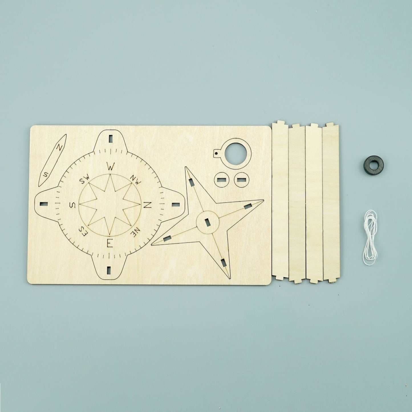 Laser-cut wood pieces, magnet, and string included in the DIY Compass Kit for kids.