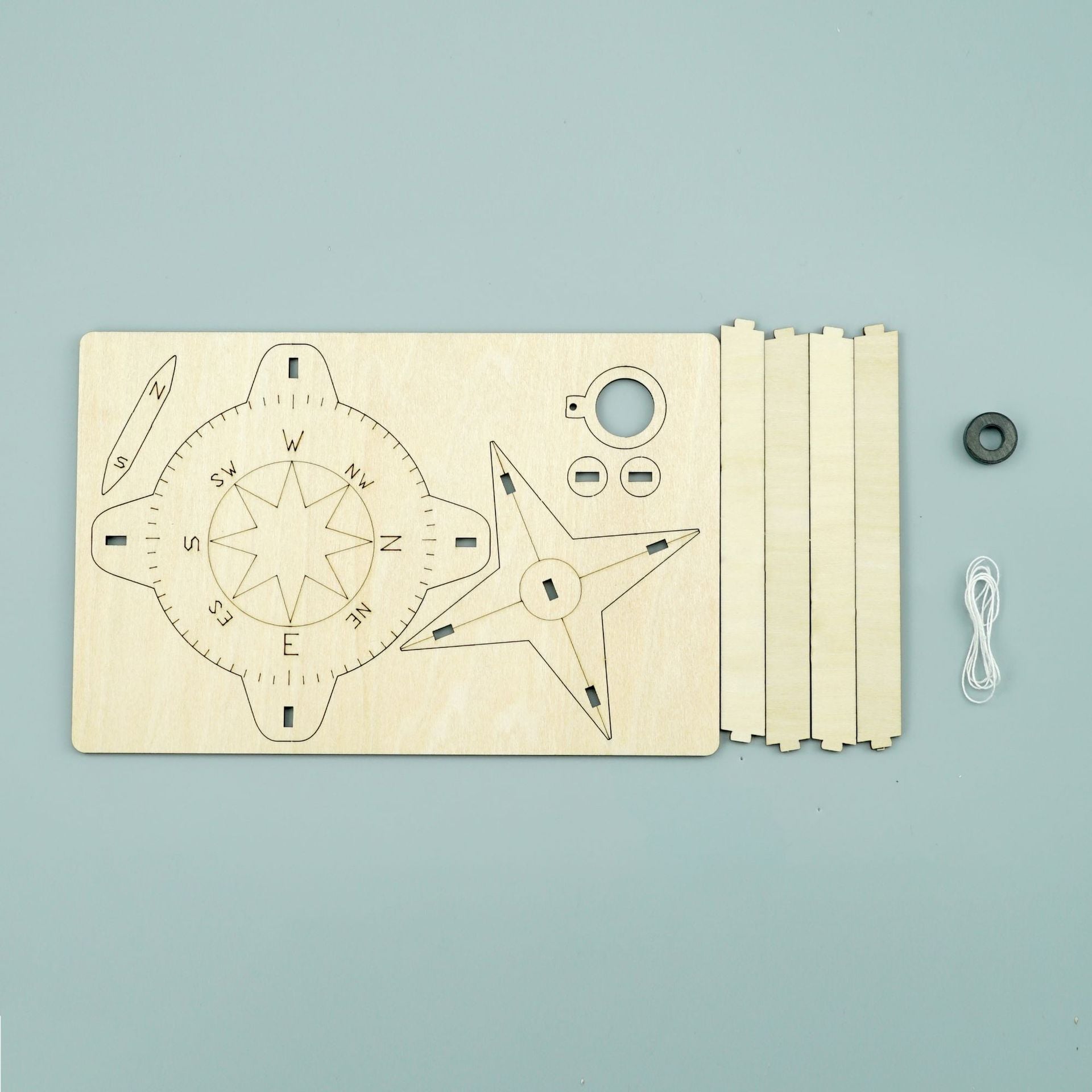 Laser-cut wood pieces, magnet, and string included in the DIY Compass Kit for kids.