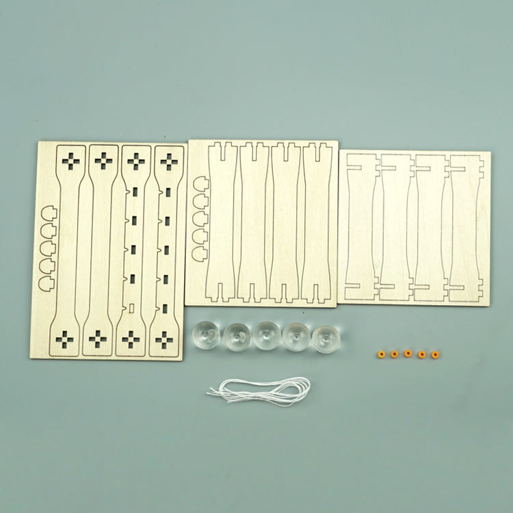 Unassembled DIY Newton's Cradle Kit components laid out: laser-cut wood pieces, clear spheres, strings, and small orange fasteners. Ready-to-build science project.