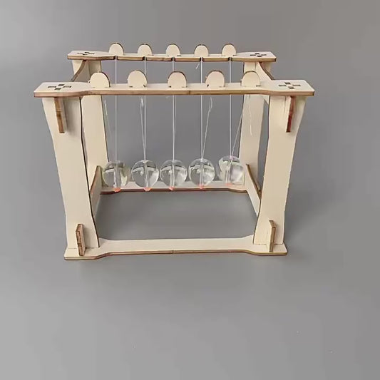 DIY Newton's Cradle Kit assembly steps shown. Wooden frame, acrylic spheres, and string components being put together. Educational STEM toy.